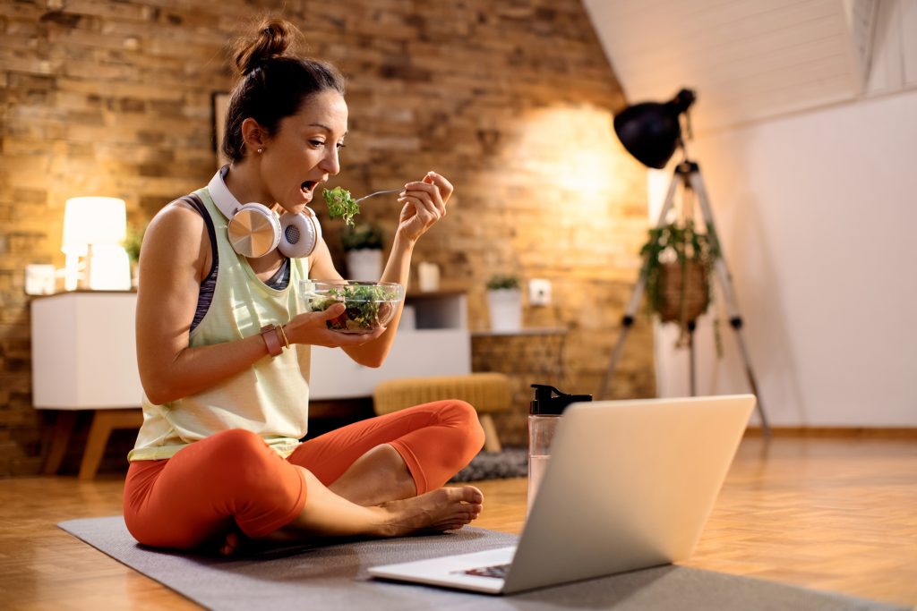 female athlete eating salad using laptop after working out home scaled