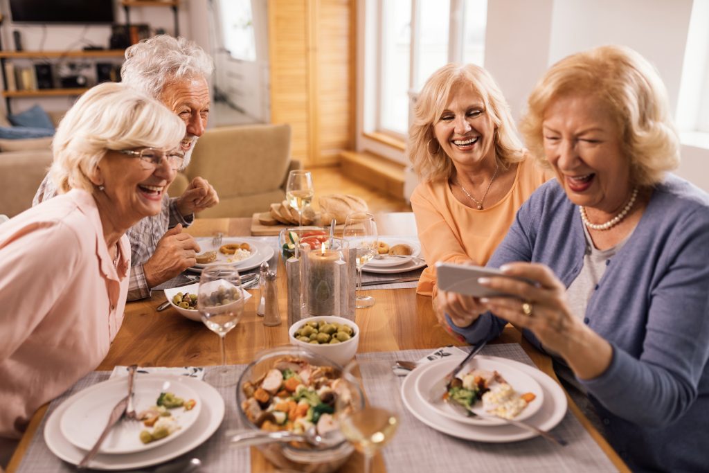 group happy senior friends laughing while watching something funny mobile phone lunch time scaled