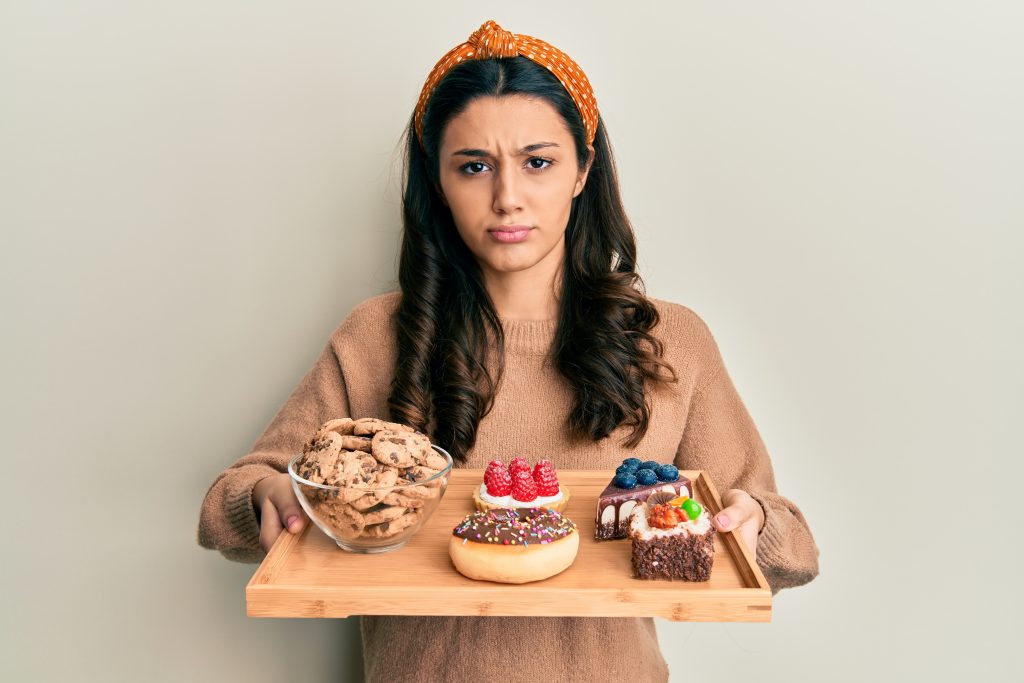 young hispanic woman holding tray with pastries breakfast skeptic nervous frowning upset because problem negative person scaled