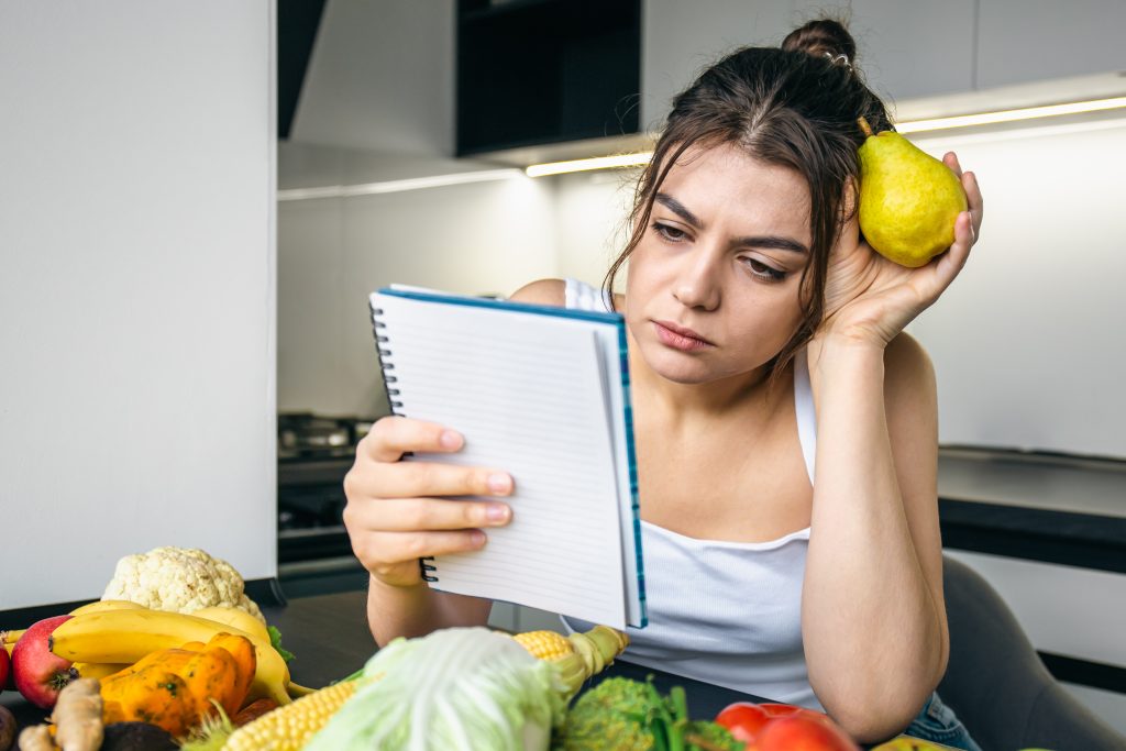 young woman kitchen with notebook vegetables scaled