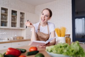 young beautiful woman kitchen apron writes down her favorite recipes fresh vegetables scaled